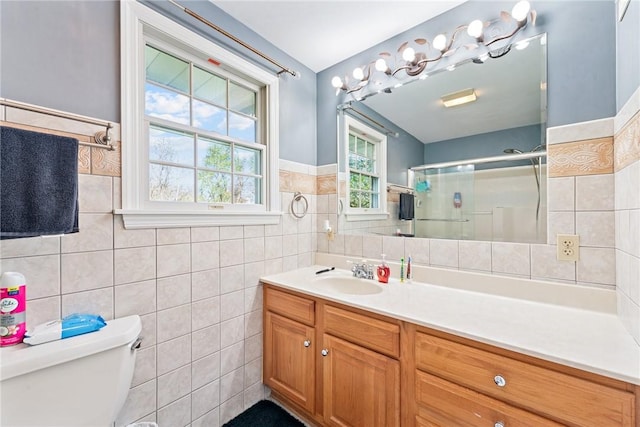 bathroom with tile walls, a shower stall, toilet, vanity, and a wainscoted wall