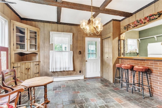 doorway to outside with baseboard heating, wood walls, stone tile flooring, beamed ceiling, and a chandelier