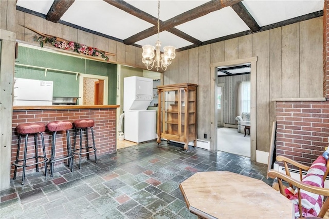 dining room featuring stacked washing machine and dryer, wood walls, stone tile floors, coffered ceiling, and beamed ceiling