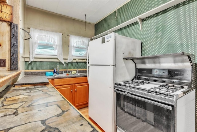 kitchen featuring range with gas stovetop, a sink, brown cabinetry, and freestanding refrigerator