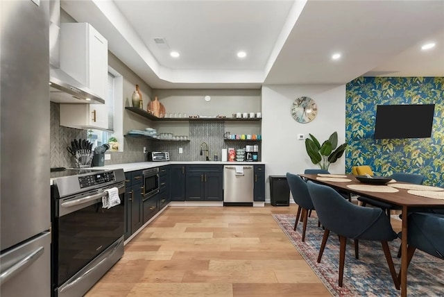 kitchen with appliances with stainless steel finishes, open shelves, wallpapered walls, a sink, and light countertops