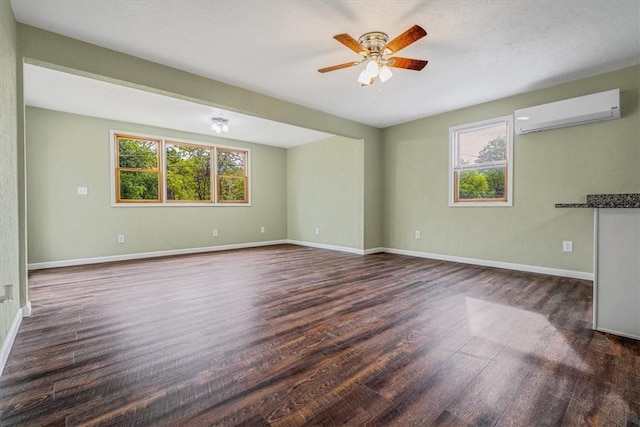 spare room featuring a wall mounted air conditioner, dark wood-style floors, a ceiling fan, and baseboards