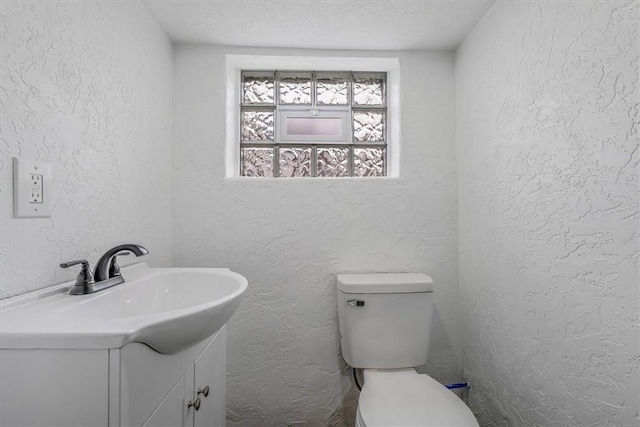 half bath featuring vanity, toilet, and a textured wall