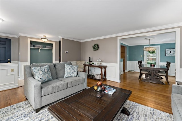 living area with wood finished floors, ornamental molding, a wainscoted wall, a chandelier, and a decorative wall