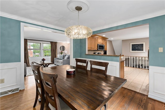dining space with a chandelier, wainscoting, crown molding, and light wood-style floors