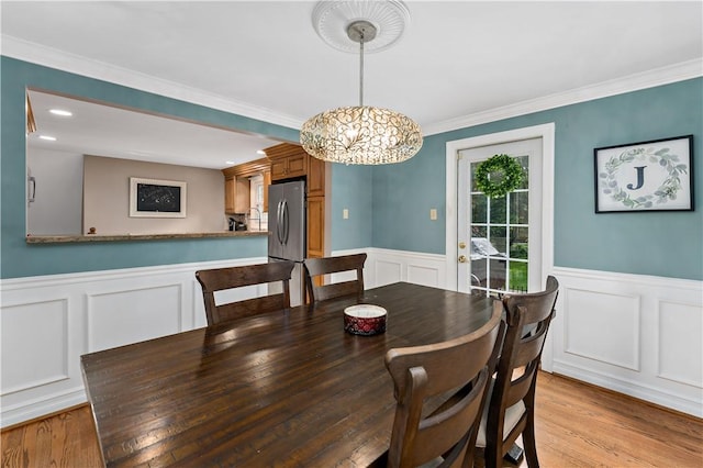 dining room featuring a decorative wall, a wainscoted wall, light wood-style floors, a chandelier, and ornamental molding