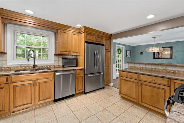 kitchen featuring appliances with stainless steel finishes, a sink, brown cabinets, decorative backsplash, and light tile patterned floors