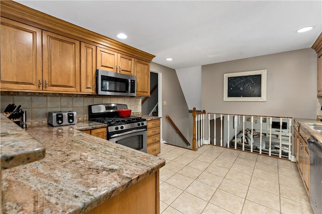 kitchen with appliances with stainless steel finishes, light stone countertops, brown cabinets, light tile patterned flooring, and decorative backsplash