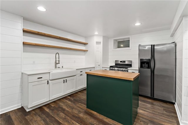 kitchen with wood counters, stainless steel appliances, open shelves, a sink, and a center island