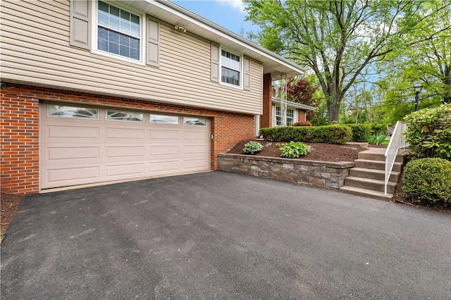 view of side of property with brick siding, an attached garage, stairway, and asphalt driveway