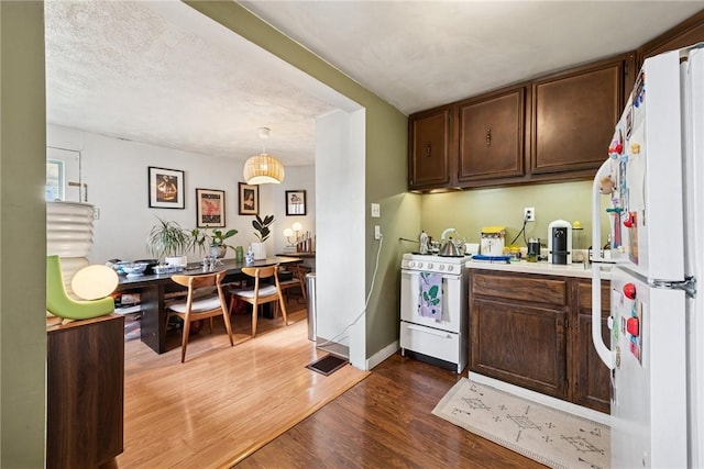 kitchen featuring white appliances, wood finished floors, dark brown cabinetry, light countertops, and hanging light fixtures