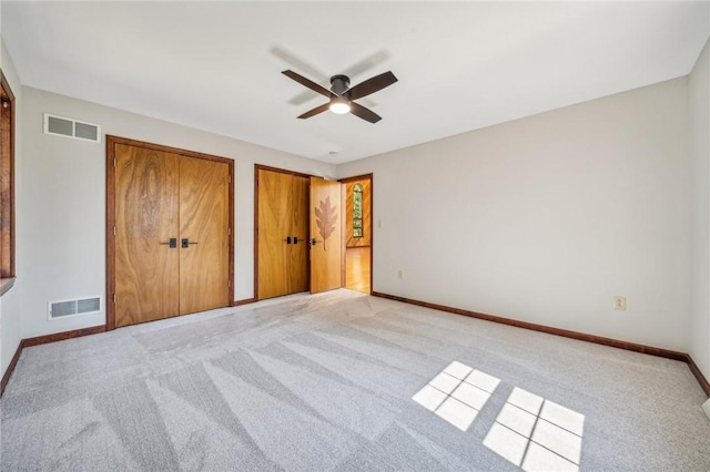 unfurnished bedroom featuring light carpet, baseboards, two closets, and ceiling fan