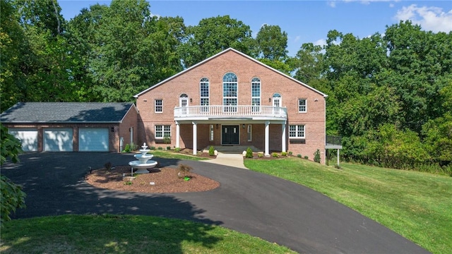 colonial inspired home featuring driveway, a front yard, a garage, a balcony, and brick siding