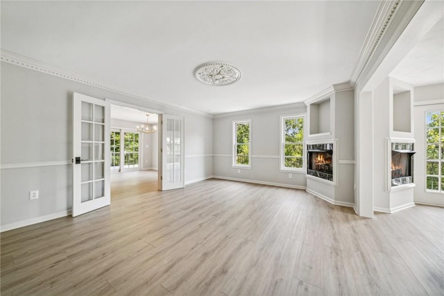 unfurnished living room with a warm lit fireplace, healthy amount of natural light, french doors, wood finished floors, and crown molding