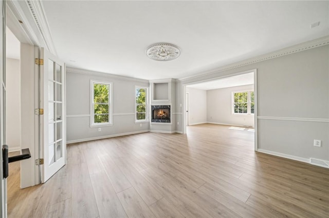 unfurnished living room with light wood-style flooring, ornamental molding, baseboards, and a lit fireplace