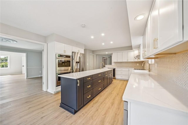kitchen featuring stainless steel appliances, white cabinets, a kitchen island with sink, light wood finished floors, and a sink