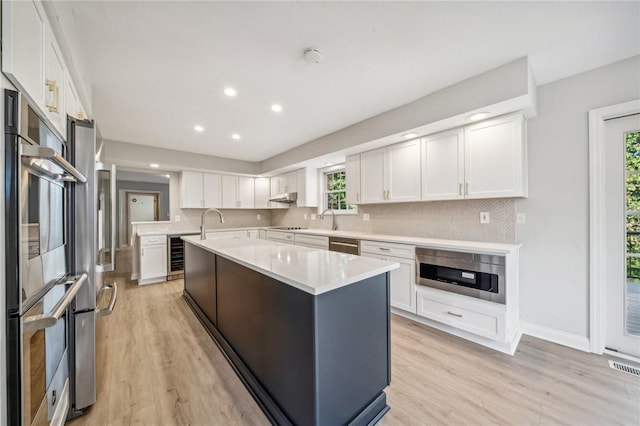 kitchen with light countertops, a kitchen island, decorative backsplash, light wood finished floors, and white cabinetry