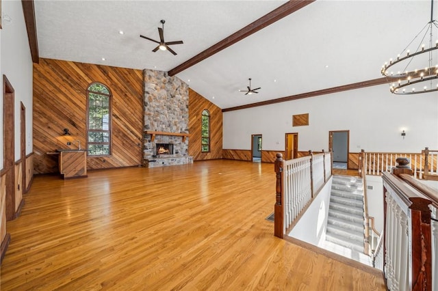 unfurnished living room with a ceiling fan, wooden walls, a fireplace, a chandelier, and light wood finished floors