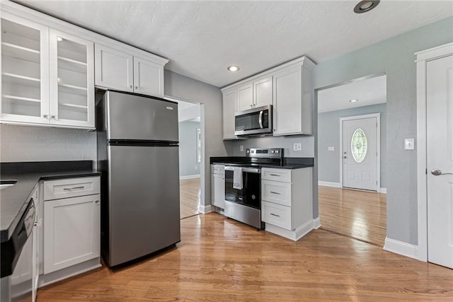 kitchen with stainless steel appliances, dark countertops, white cabinetry, glass insert cabinets, and recessed lighting