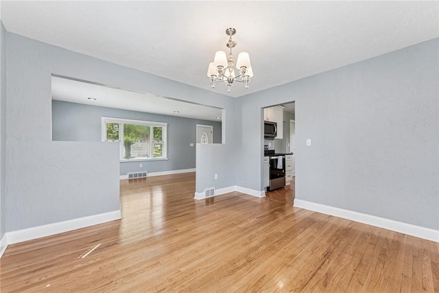 spare room with a chandelier, light wood-type flooring, and baseboards