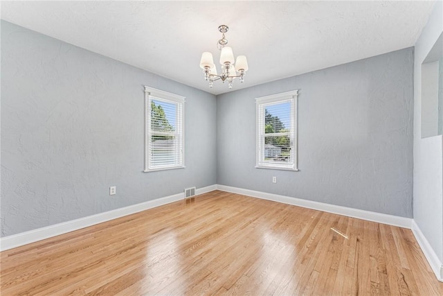 unfurnished room featuring healthy amount of natural light, a chandelier, and light wood-type flooring