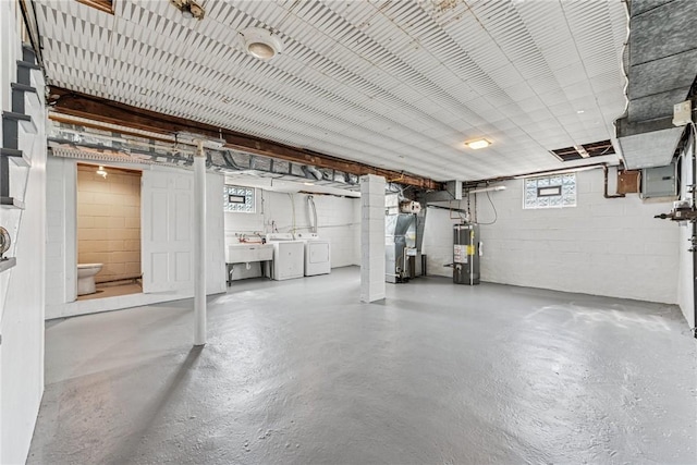 below grade area featuring gas water heater, washing machine and clothes dryer, concrete block wall, a sink, and plenty of natural light