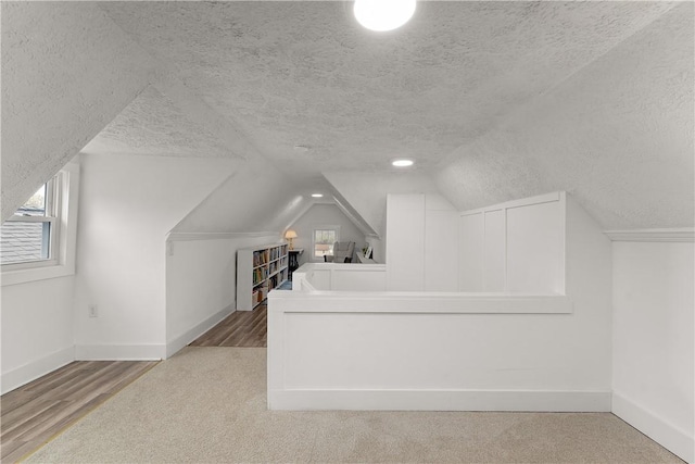 bonus room with a textured ceiling, baseboards, vaulted ceiling, and carpet