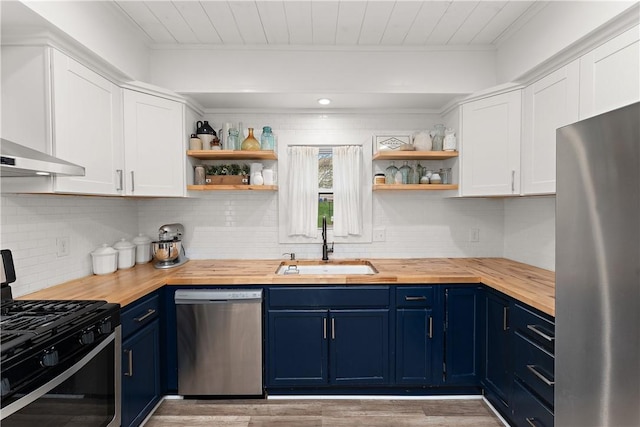 kitchen with stainless steel appliances, blue cabinets, butcher block counters, a sink, and open shelves