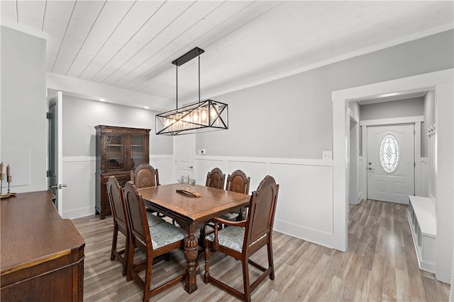 dining space with wainscoting, light wood finished floors, a chandelier, wooden ceiling, and a decorative wall