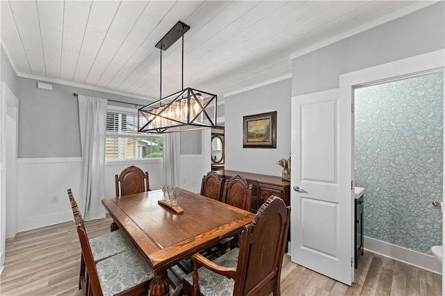 dining area with light wood-style floors, a wainscoted wall, a chandelier, wooden ceiling, and wallpapered walls