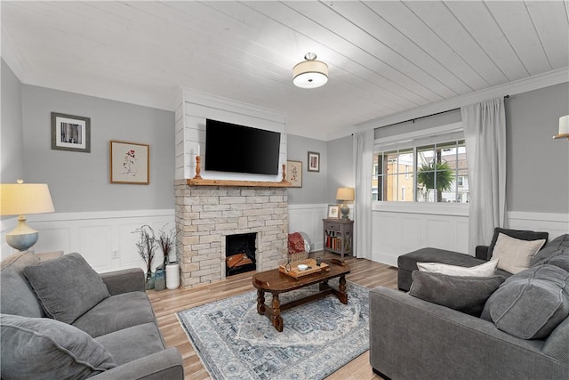 living room with wood finished floors, wainscoting, a fireplace, and crown molding