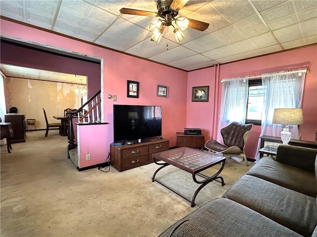 carpeted living area with ceiling fan and stairs