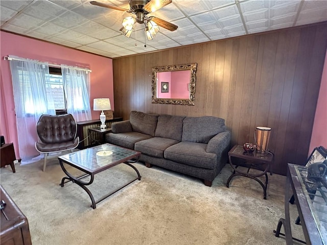 living room featuring carpet flooring, a ceiling fan, wooden walls, and an ornate ceiling