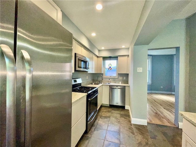 kitchen featuring stainless steel appliances, light countertops, a sink, white cabinetry, and baseboards