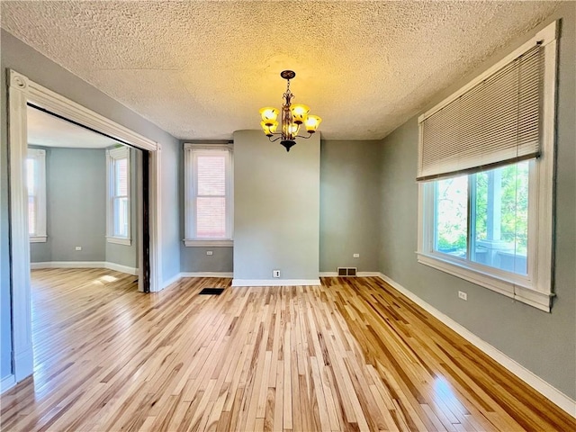 unfurnished dining area with wood finished floors, a chandelier, a textured ceiling, and baseboards