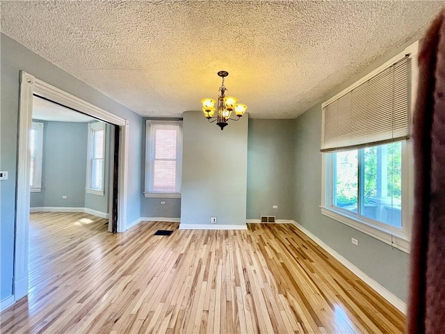 unfurnished dining area with light wood finished floors, a chandelier, a textured ceiling, and baseboards