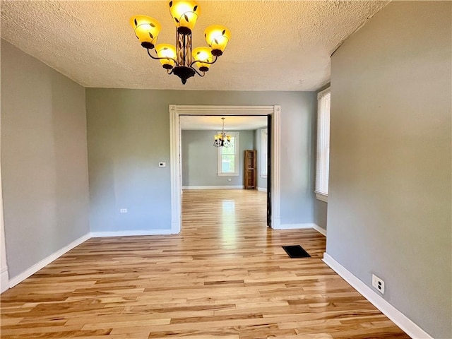 unfurnished dining area featuring a chandelier, light wood finished floors, baseboards, and a textured ceiling