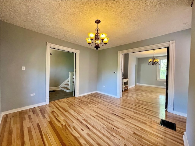 unfurnished dining area featuring a chandelier, light wood finished floors, baseboards, and a textured ceiling
