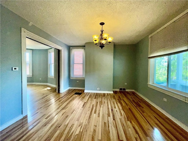 unfurnished dining area featuring hardwood / wood-style flooring, a chandelier, a textured ceiling, and baseboards