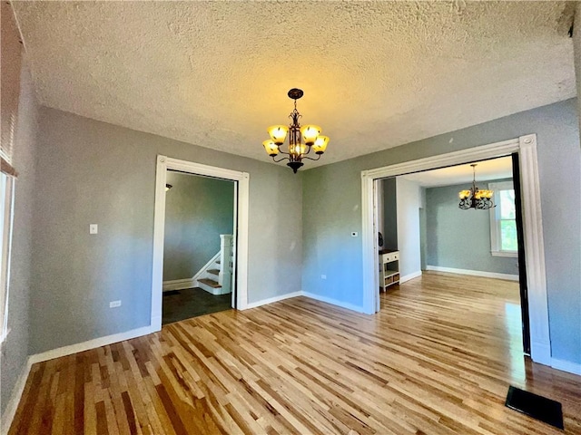 unfurnished dining area with a chandelier, wood finished floors, baseboards, a textured ceiling, and stairs