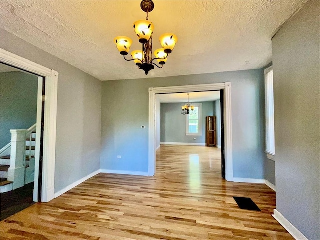 unfurnished dining area featuring a chandelier, wood finished floors, stairs, baseboards, and a textured ceiling