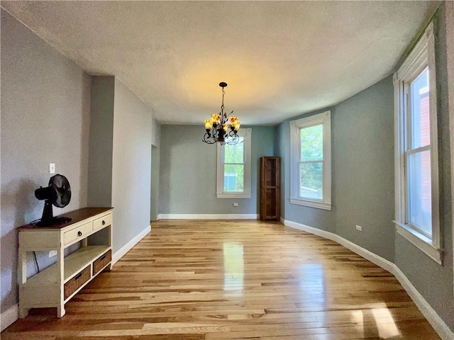 unfurnished dining area featuring wood finished floors, a chandelier, baseboards, and a textured ceiling