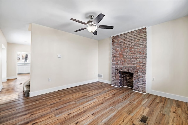 unfurnished living room featuring wood finished floors, a ceiling fan, a brick fireplace, and baseboards