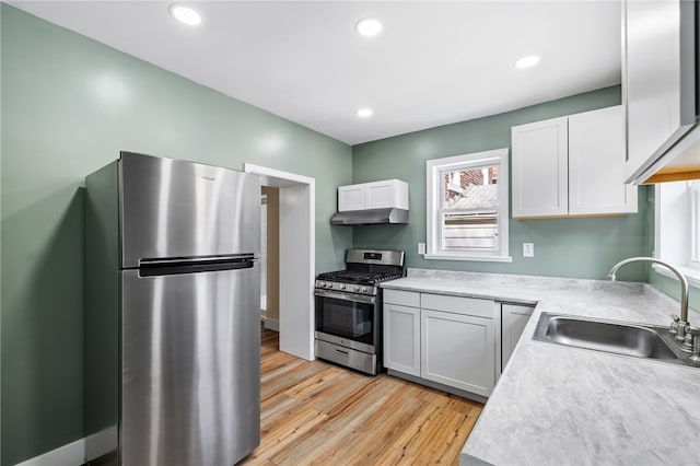 kitchen with stainless steel appliances, a sink, light countertops, light wood finished floors, and white cabinets