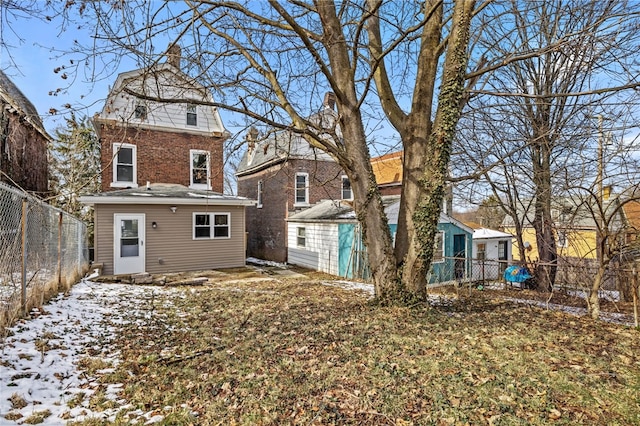 snow covered rear of property featuring a fenced backyard, an outdoor structure, and brick siding