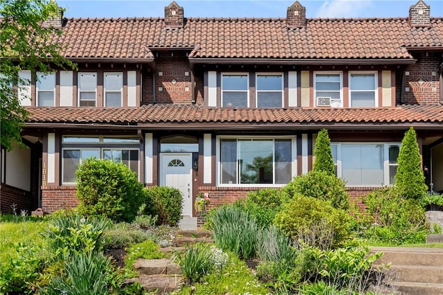 view of front of property featuring a tiled roof, brick siding, and a chimney