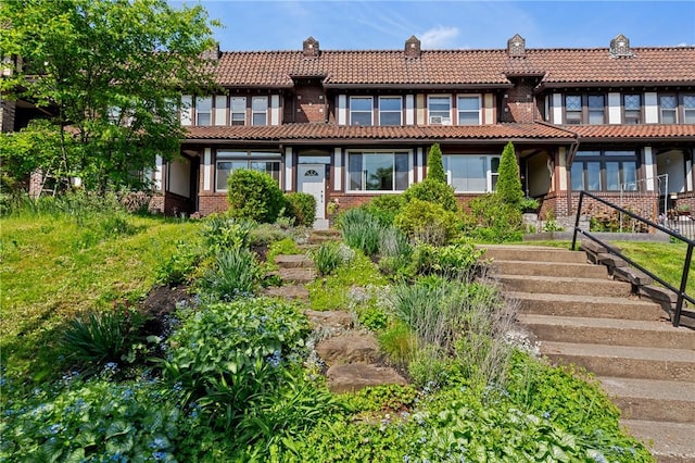 view of front of house featuring a tiled roof, brick siding, and stairway