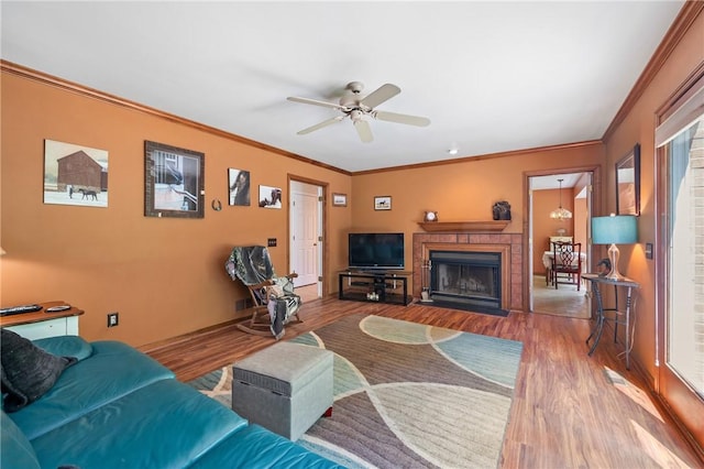living room with wood finished floors, ornamental molding, a fireplace with flush hearth, ceiling fan, and plenty of natural light