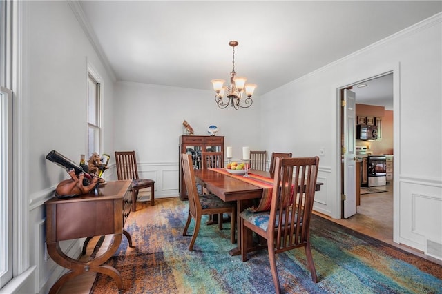 dining room featuring ornamental molding, a chandelier, a decorative wall, a wainscoted wall, and wood finished floors