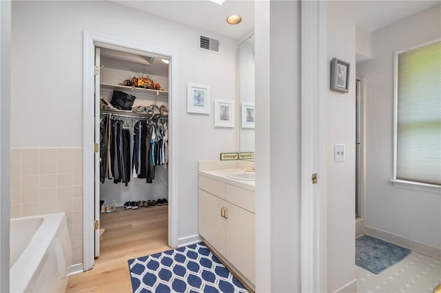 bathroom featuring vanity, wood finished floors, a garden tub, a spacious closet, and tile walls